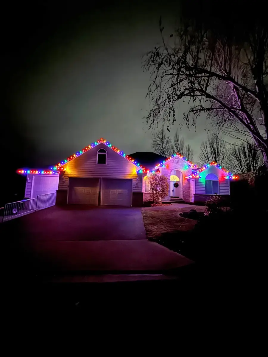 Two-story home with multicolor Christmas lights running along every roofline at night