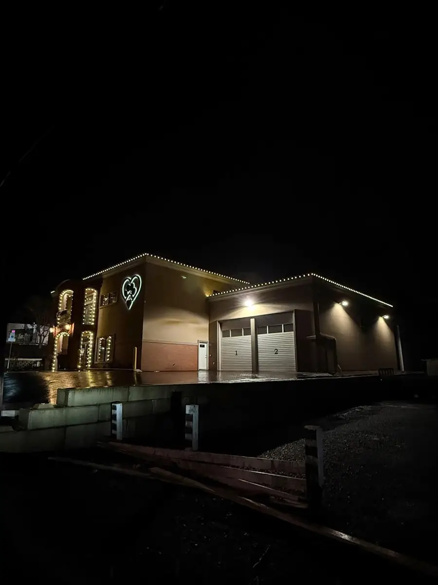 Commercial building at night with warm white lights along the rooflines and a lit heart sign